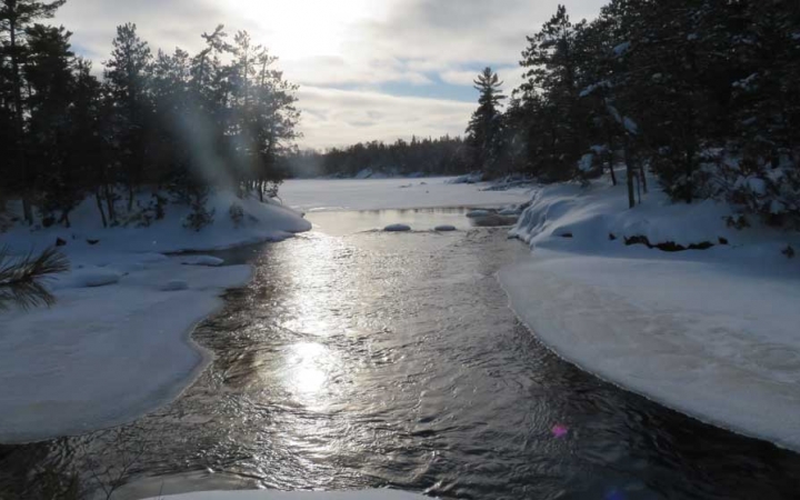 a river flows through a snowy landscape withe trees lining the shore.